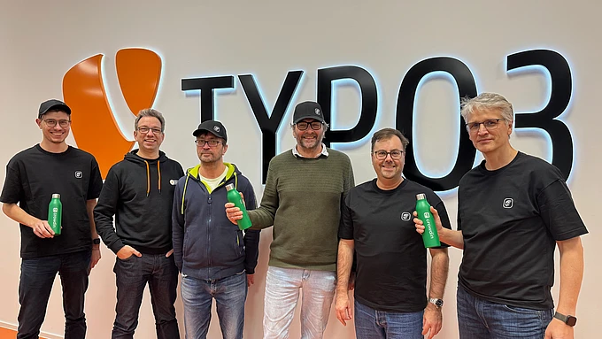 Members of the TYPO3 Localization Team standing in front of a big TYPO3 logo on a wall